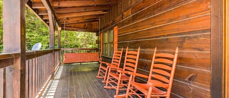 Un porche de madera con mecedoras, una terraza de madera y vistas al verdor.