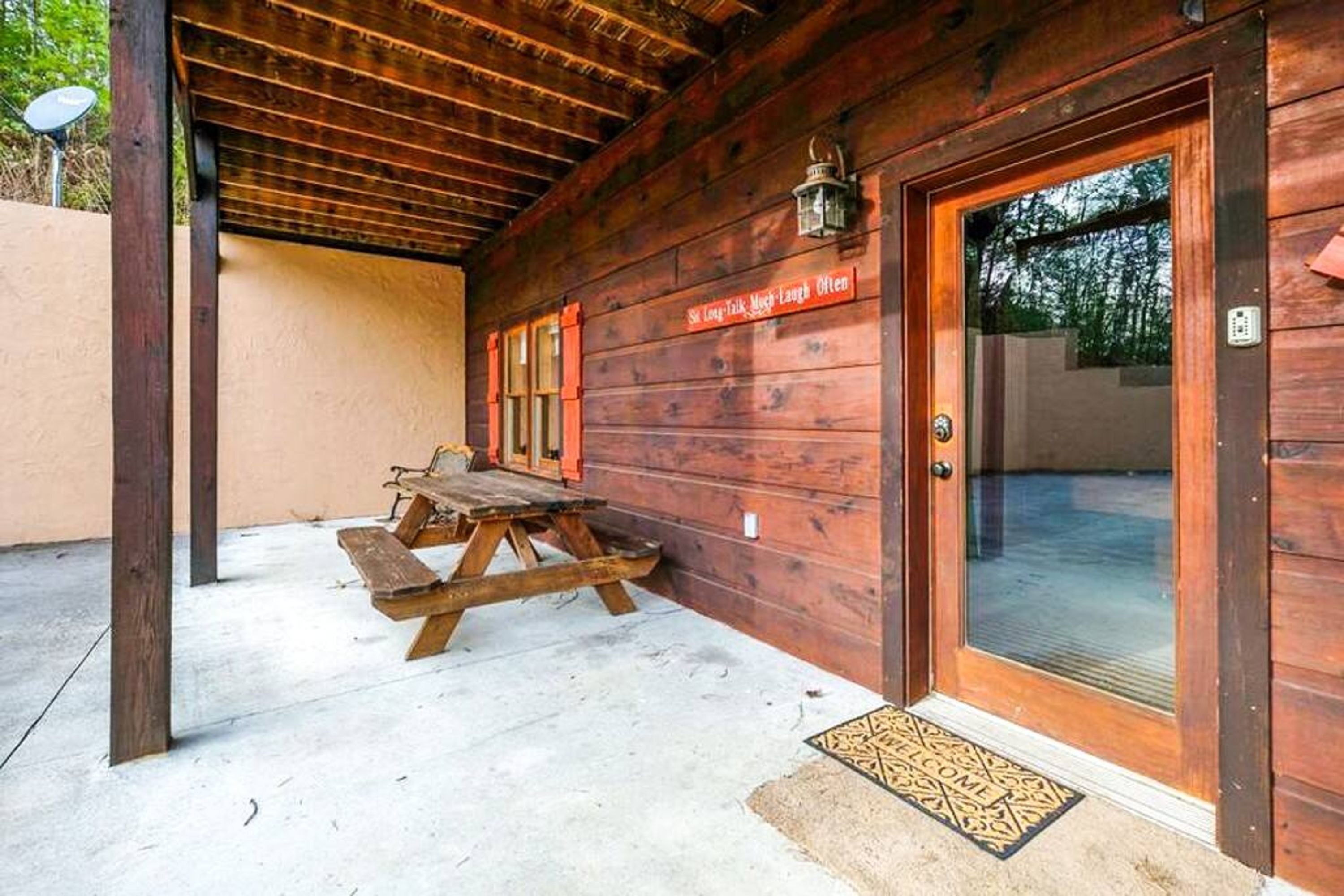 Una cabaña de madera con una mesa de picnic afuera, una puerta con felpudo y un letrero sobre la puerta.