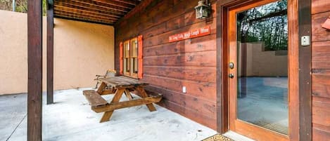 Una cabaña de madera con una mesa de picnic afuera, una puerta con felpudo y un letrero sobre la puerta.