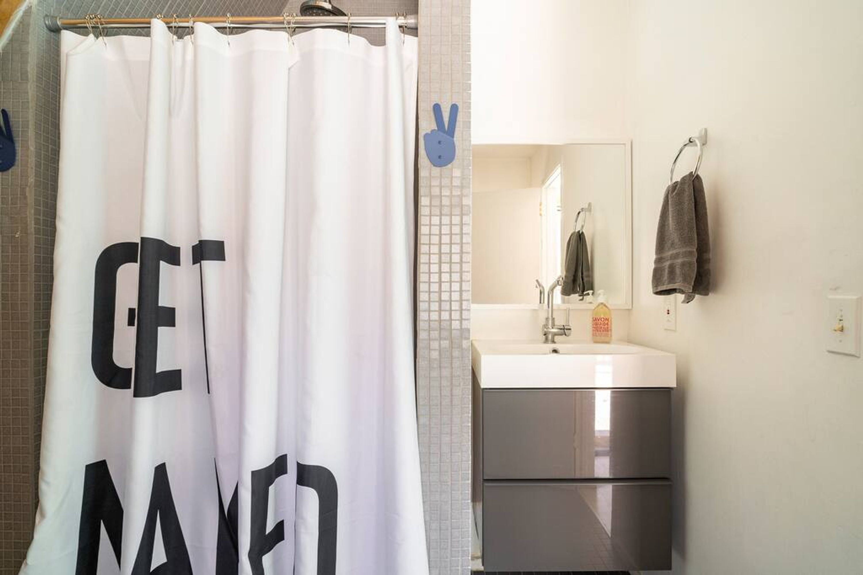 A bathroom with a shower curtain that reads "GET DRESSED," a sink with a mirror, and a towel hanging on the wall.