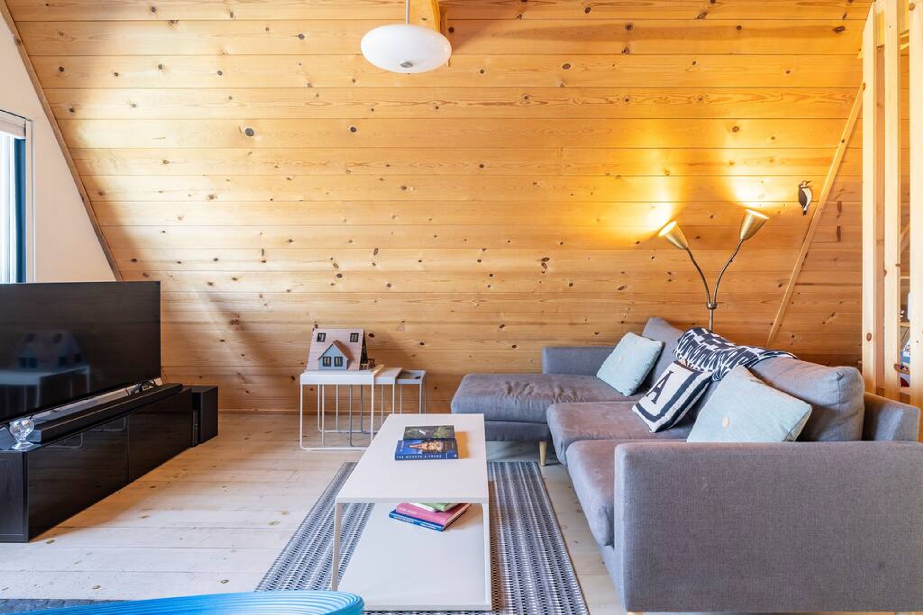 A cozy living room with a wooden ceiling, a grey sofa, a white coffee table, and a TV on a black stand.