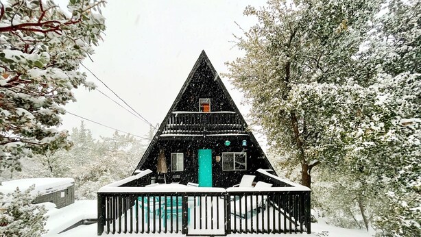 Une cabane triangulaire recouverte de neige, dotée d’un balcon et d’une porte.
