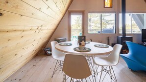 Une pièce chaleureuse avec un plafond en pente en bois, une table ronde entourée de chaises, un canapé bleu et de grandes fenêtres donnant sur l’extérieur.