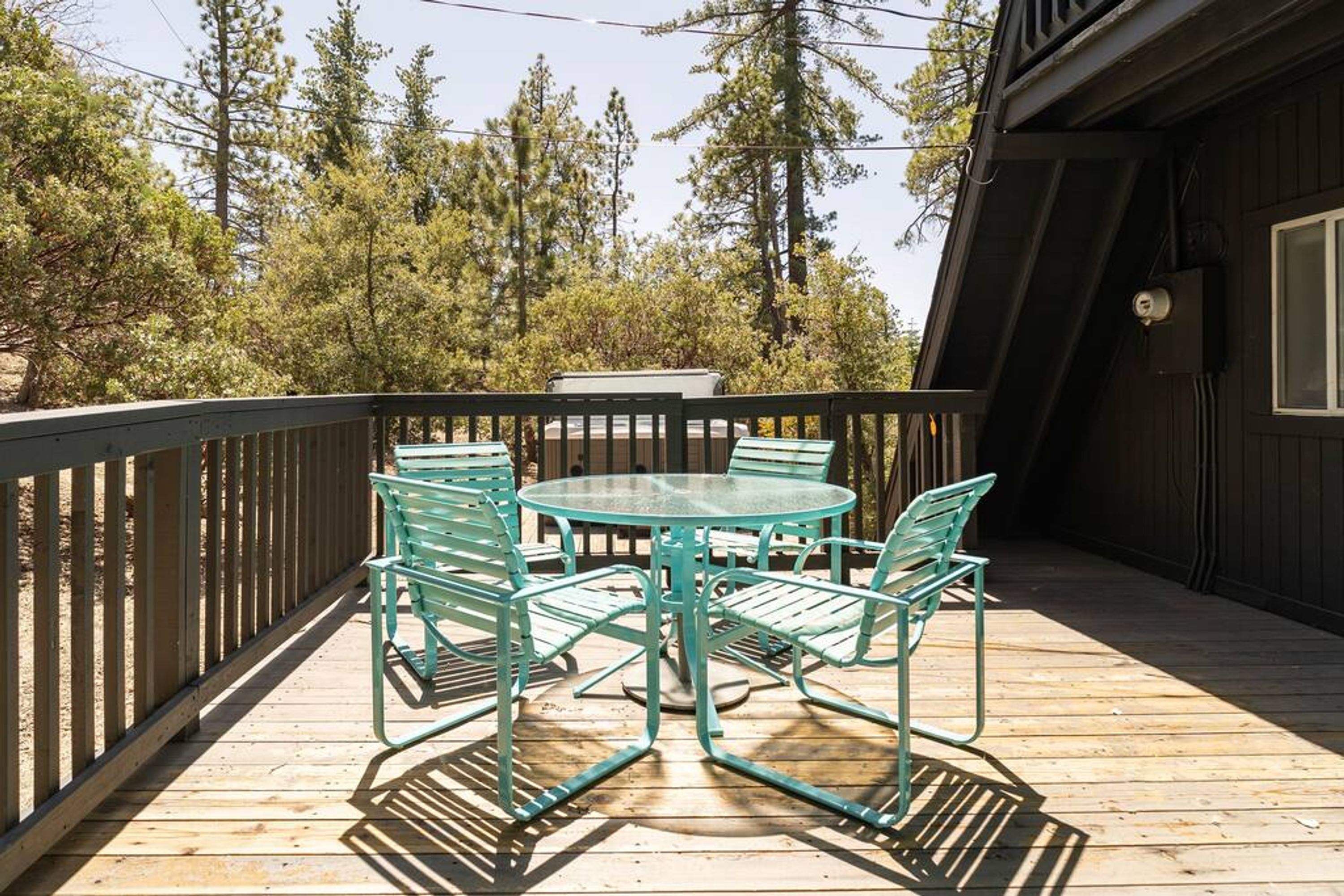 A wooden deck with a glass-top table and four chairs, surrounded by a wooden railing.