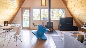 Une pièce chaleureuse aux murs lambrissés, avec une table à manger, des chaises, un fauteuil bleu, un téléviseur et une cheminée.