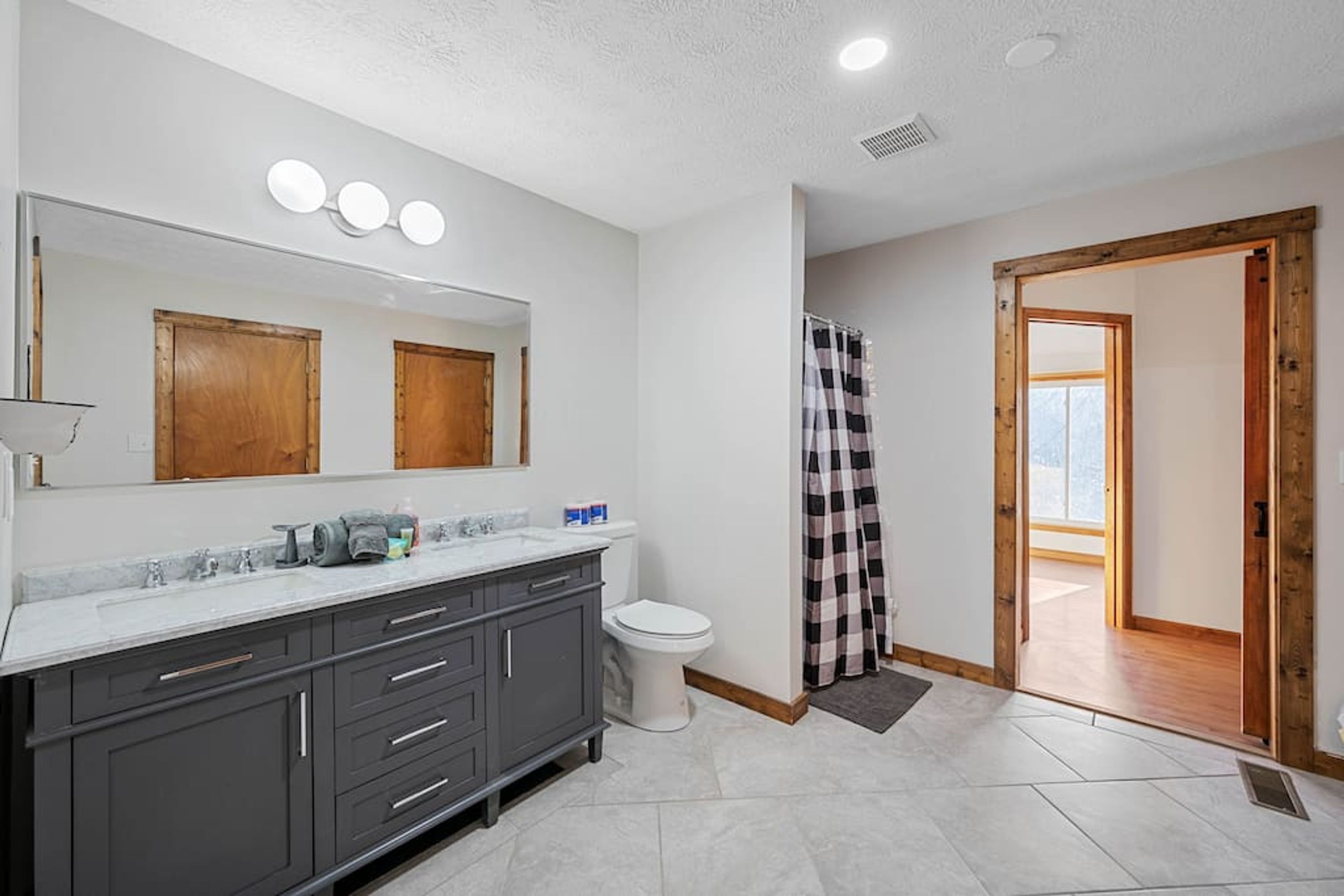 A bathroom with a large mirror, a sink, a toilet, and a shower area.