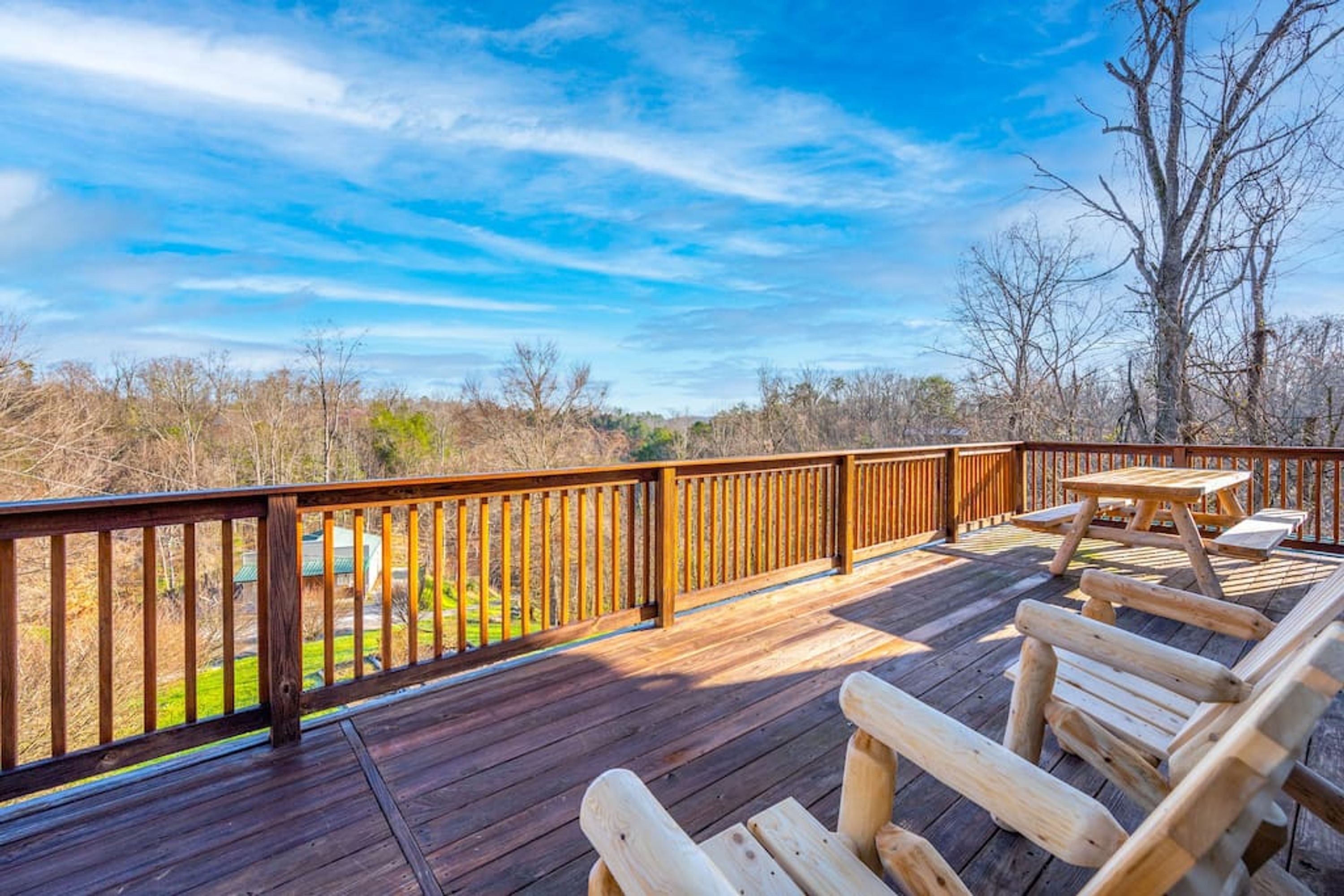 Una terraza de madera con mesa y sillas de picnic, con vista a un paisaje natural.