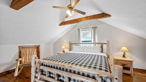 Un dormitorio con estructura de cama de madera, ventilador de techo, una ventana y dos mesitas de noche con lámparas.