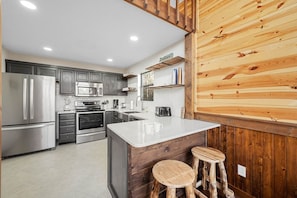 A modern kitchen with stainless steel appliances, a central island with stools, and wooden paneling on one wall. - Dog Friendly Views Hot Tub Close to PF Gsmnp (Sevierville)