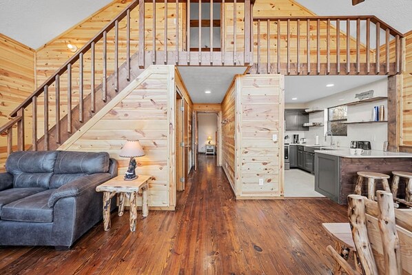 Un vaste espace de vie avec un escalier menant à une mezzanine, une cuisine moderne et un coin salon confortable avec un canapé en cuir et une petite table.