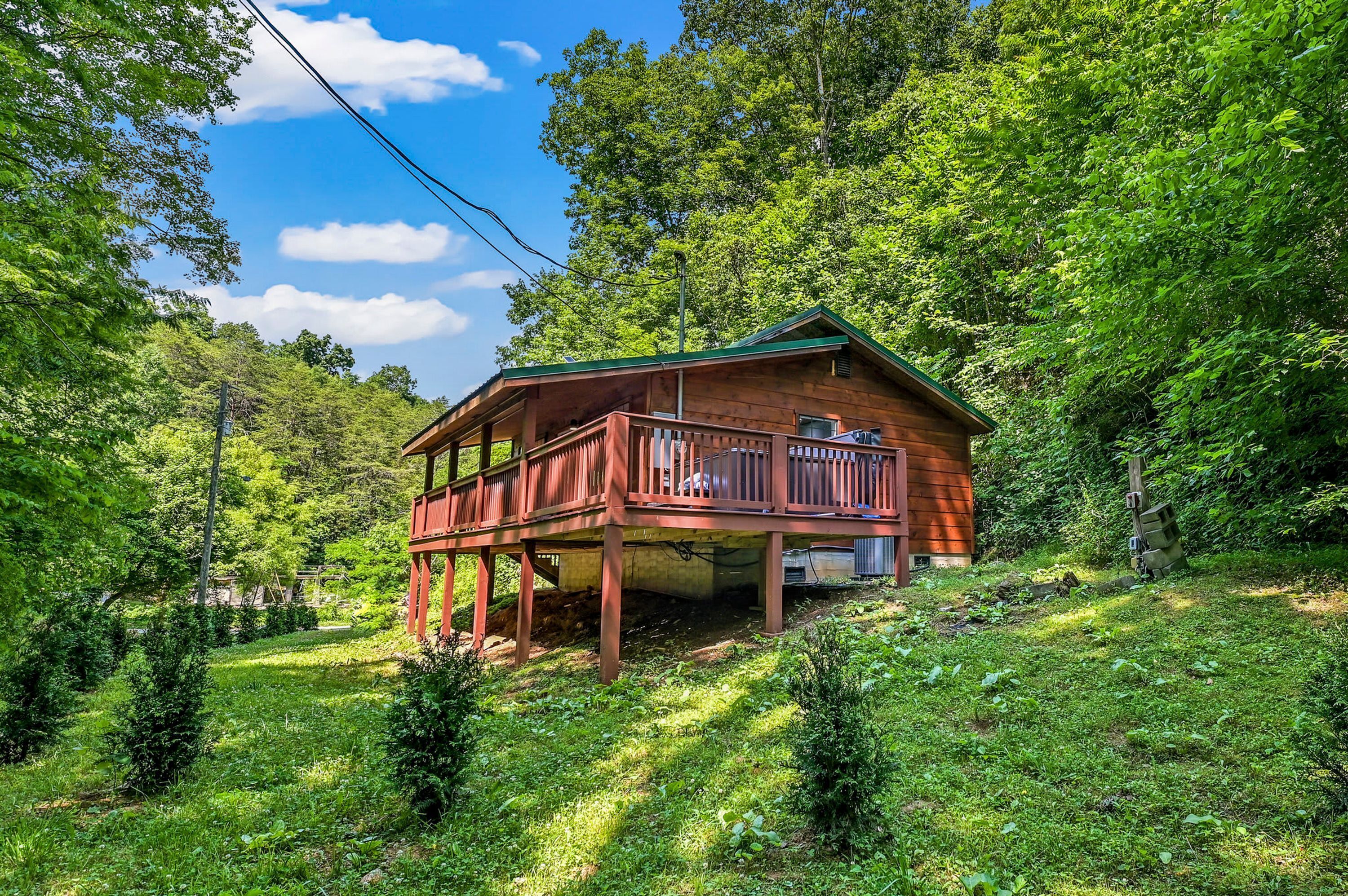 A wooden cabin with a balcony, surrounded by lush greenery and trees.