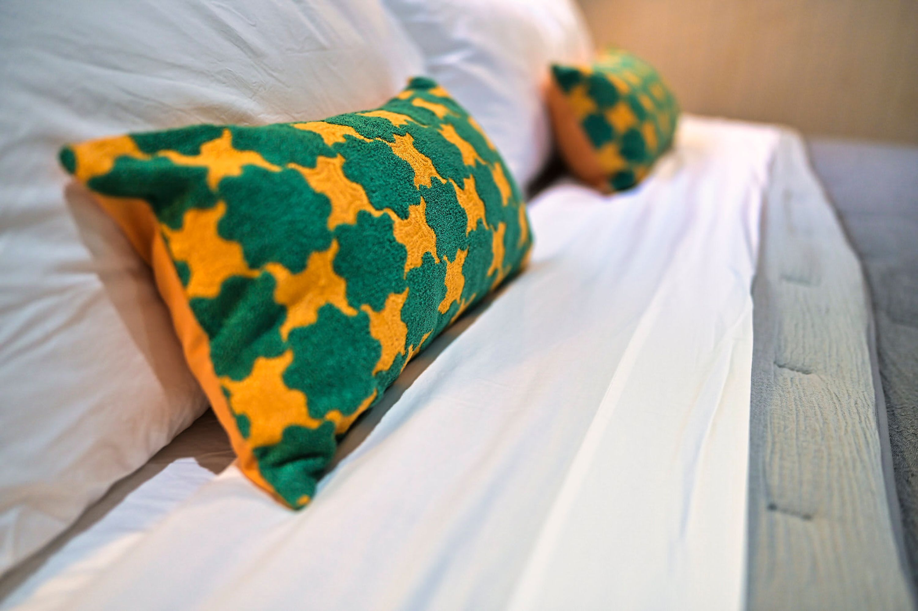 Una cama con sábanas blancas y un cojín estampado en verde y amarillo.