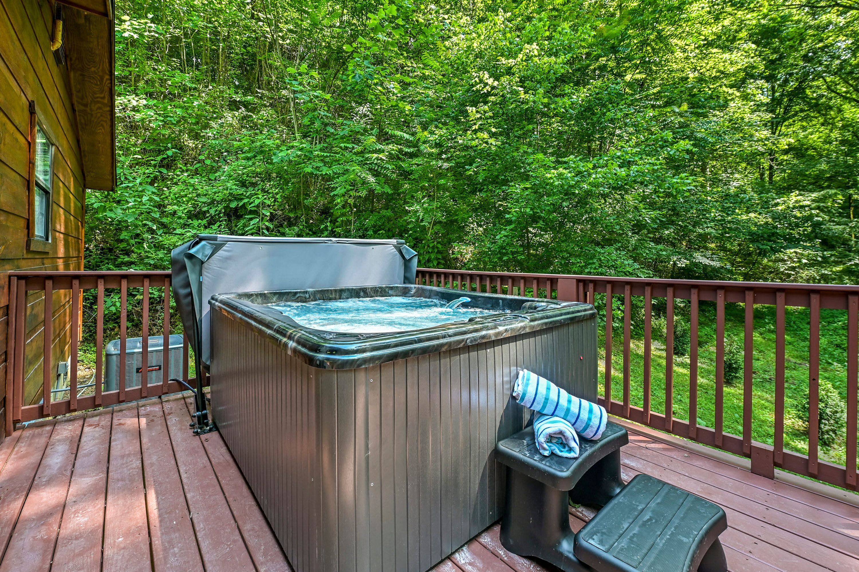 A hot tub on a wooden deck with a view of a lush green forest.