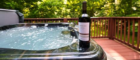 A hot tub with a bottle of wine on a wooden deck surrounded by lush greenery.