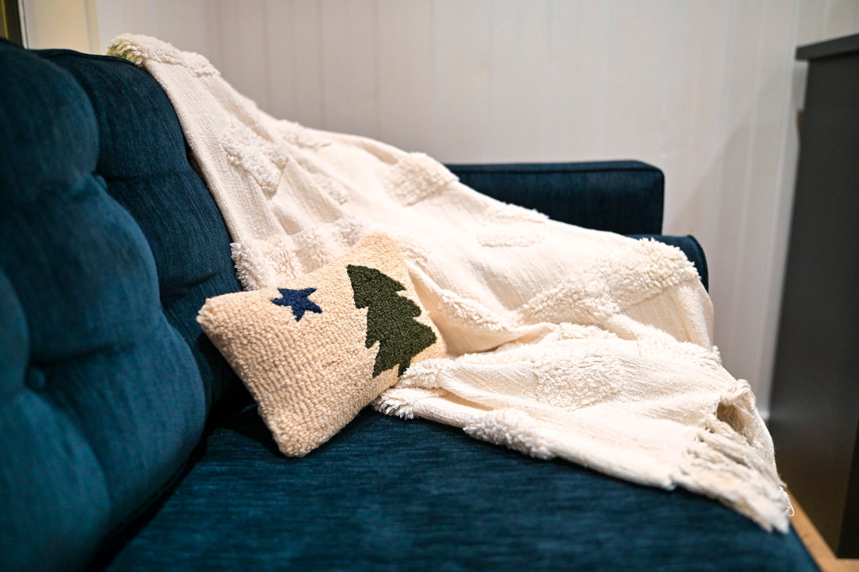 A dark blue sofa with a white blanket and a decorative pillow with a tree and star design.