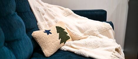 A dark blue sofa with a white blanket and a decorative pillow with a tree and star design.