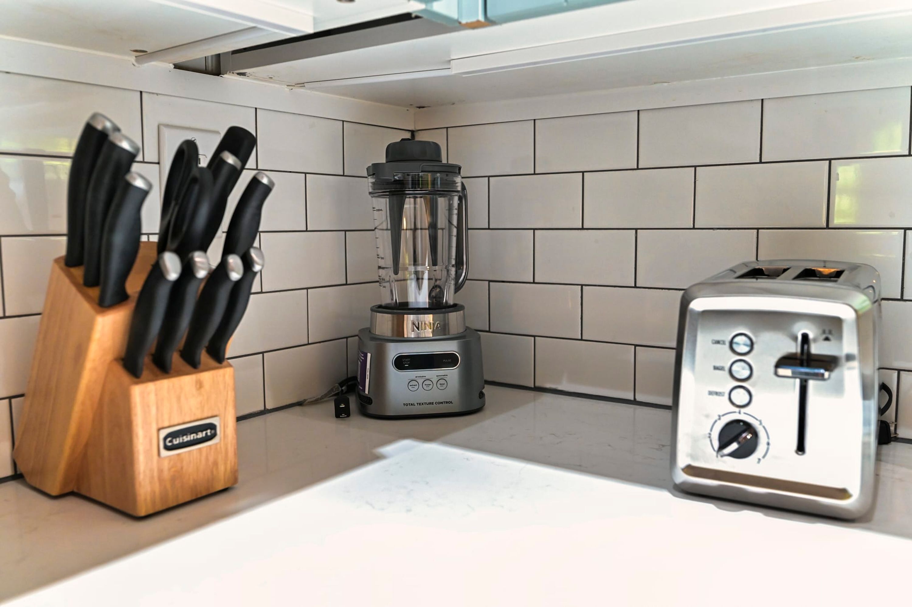 A kitchen with a blender, a toaster, and a knife block.