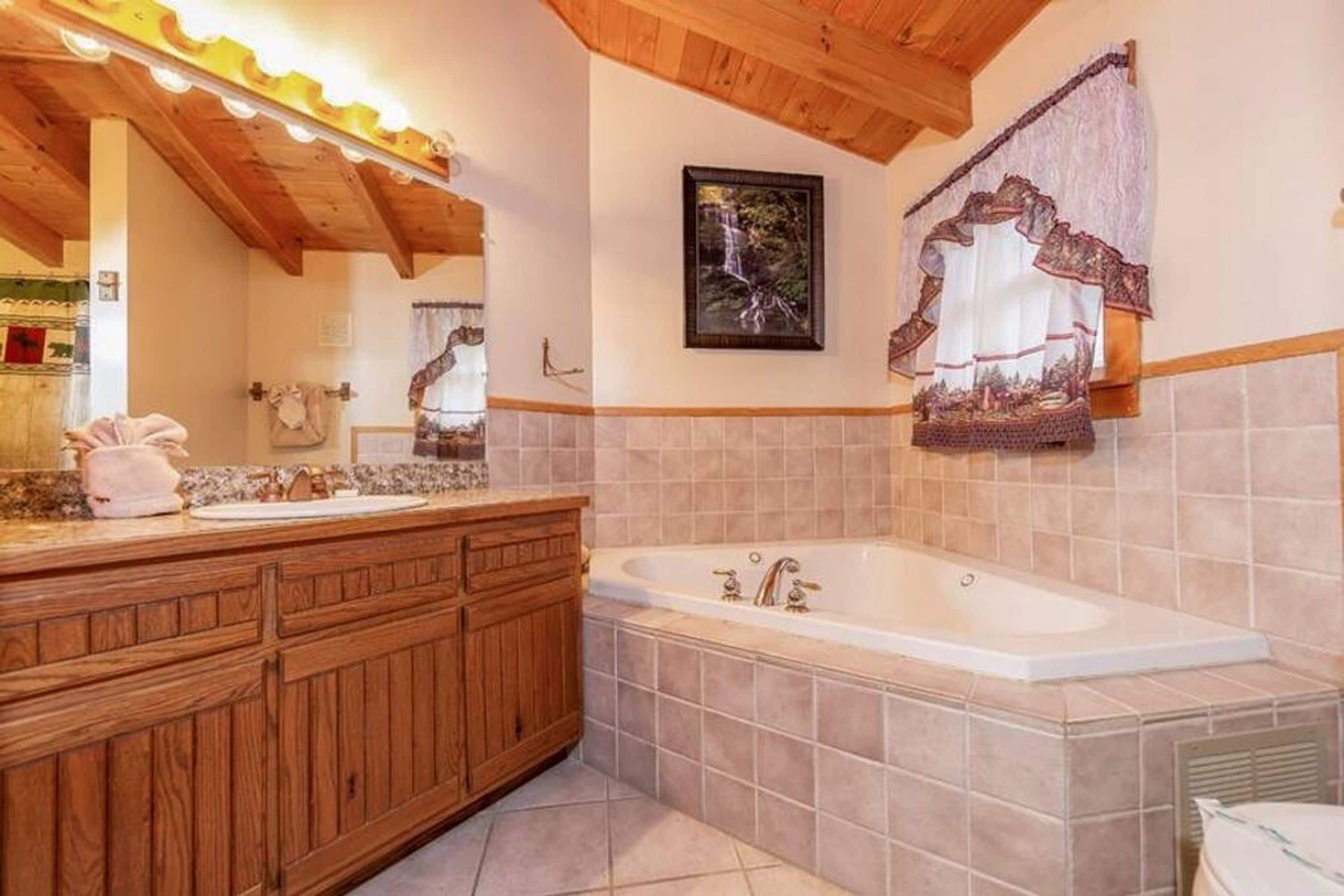 Un baño con tocador de madera, una bañera grande y un cuadro en la pared.