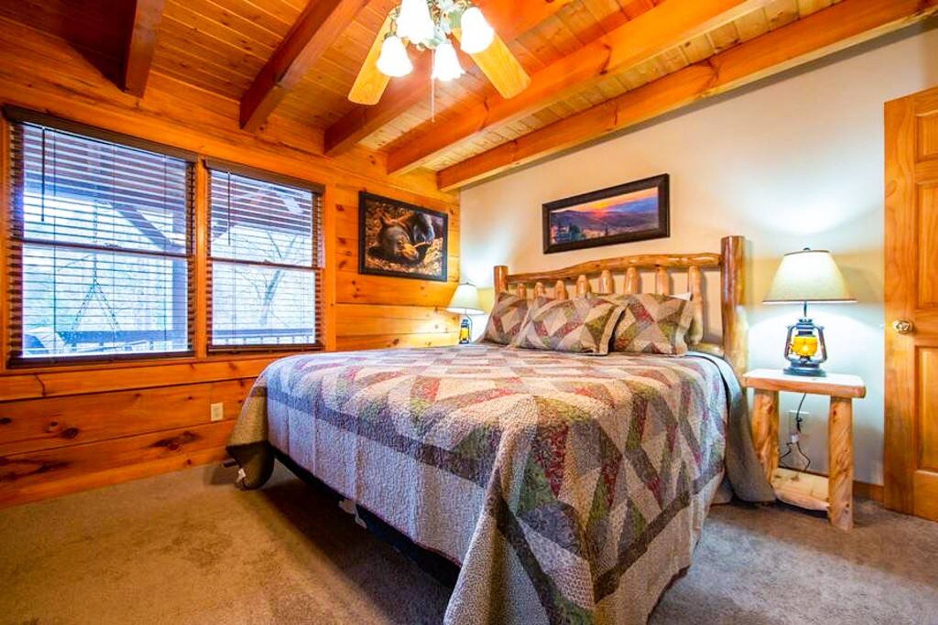 A cozy log cabin bedroom with a large bed, wooden walls, and a ceiling fan.
