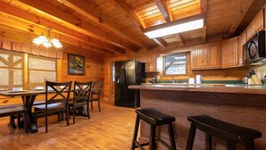 A wooden cabin interior with a kitchen area, dining table, and bar stools. - Pigeon Forge Cabin Game Room Dog Friendly Hot Tub (Pigeon Forge)
