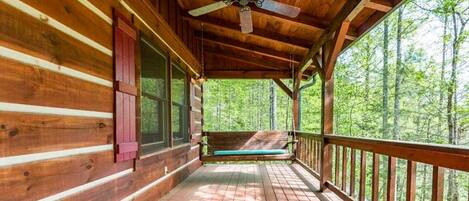 A wooden cabin with a porch, a ceiling fan, and a view of a forest.
