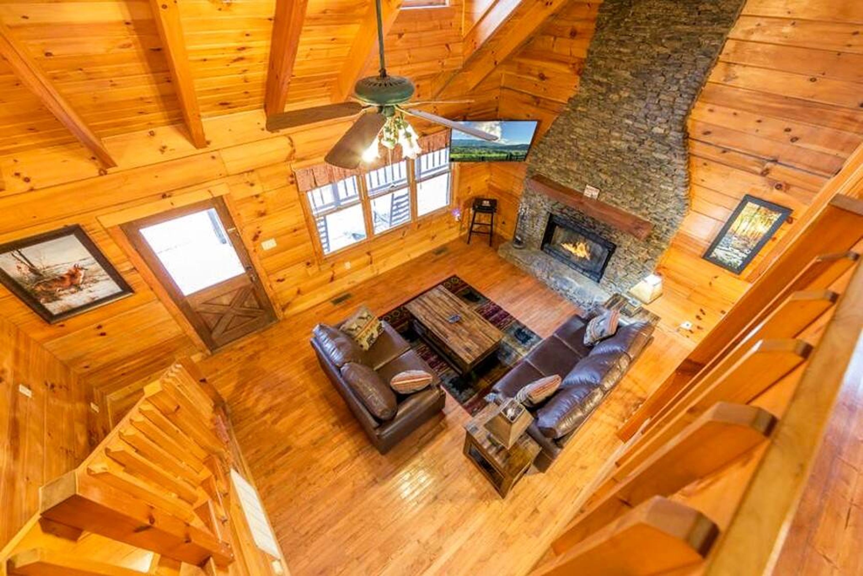 A log cabin interior with a fireplace, wooden walls, a sofa, and a ceiling fan.