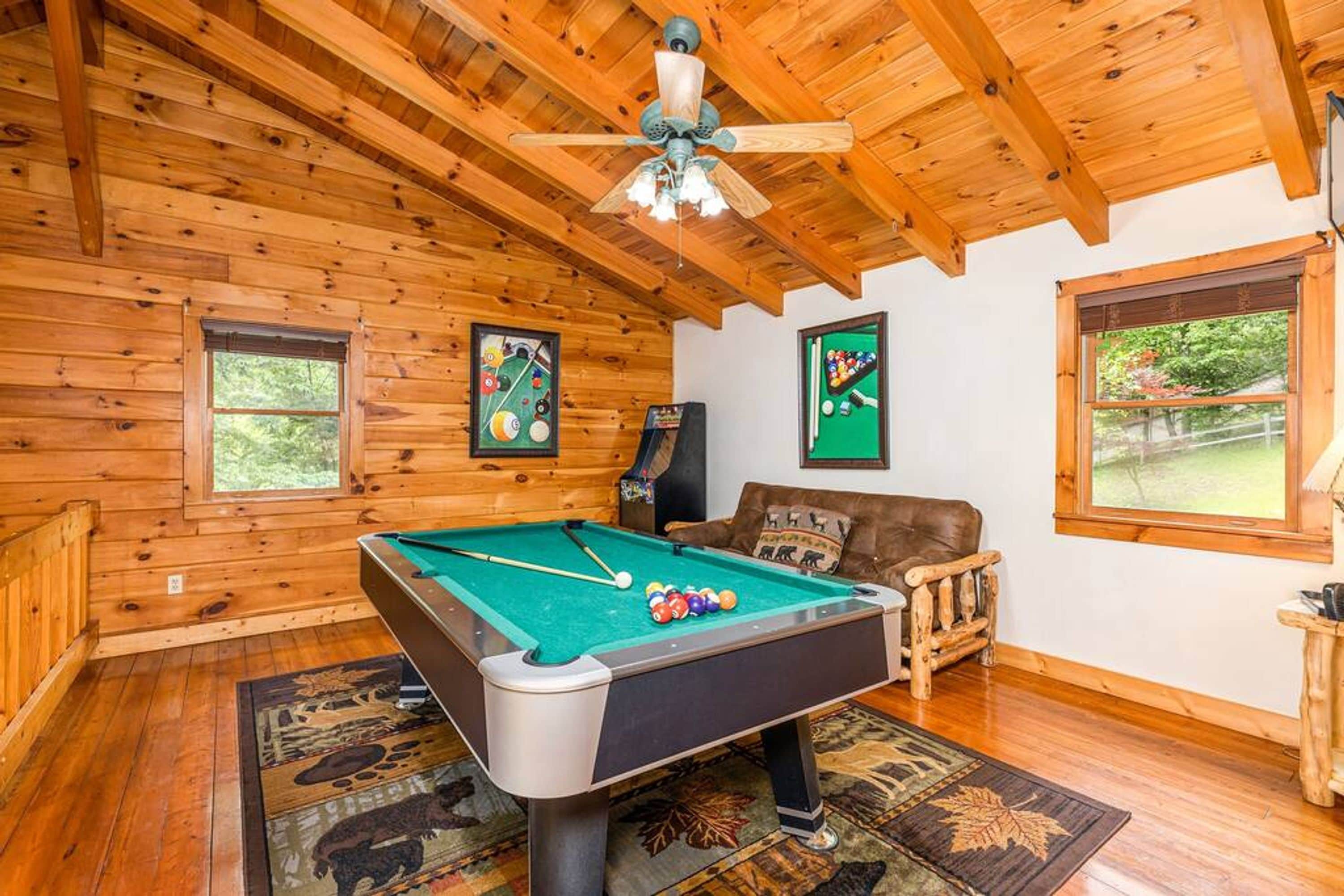 Une pièce aux murs lambrissés, équipée d’une table de billard, d’un canapé et d’un ventilateur de plafond.
