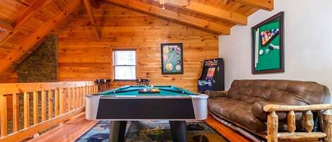 A cozy room with a pool table, a brown leather couch, and a ceiling fan.