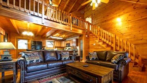 A log cabin interior with a wooden staircase, leather sofas with patterned cushions, and a wooden coffee table. - Pigeon Forge Cabin Game Room Dog Friendly Hot Tub (Pigeon Forge)
