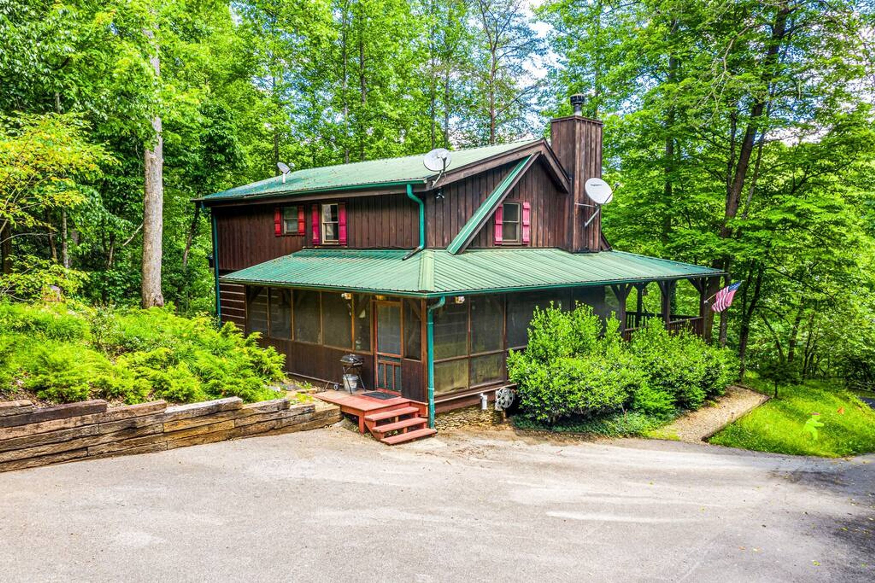 A rustic cabin with a green metal roof, large windows, and a chimney.