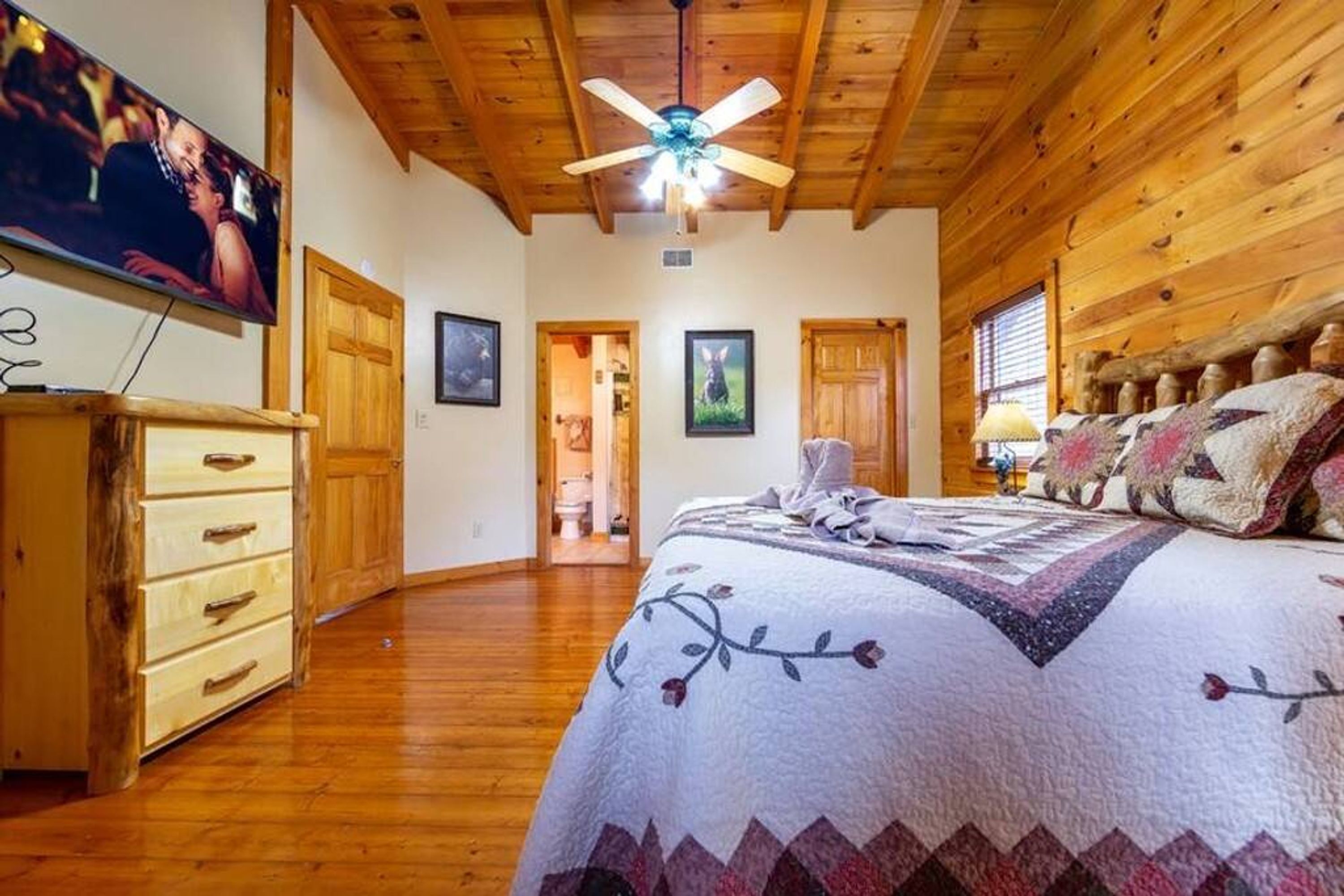 Un dormitorio acogedor con techo de madera, una cama con colcha floral, un aparador y un televisor en la pared.