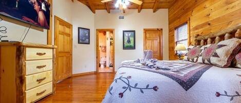 Un dormitorio acogedor con techo de madera, una cama con colcha floral, un aparador y un televisor en la pared.