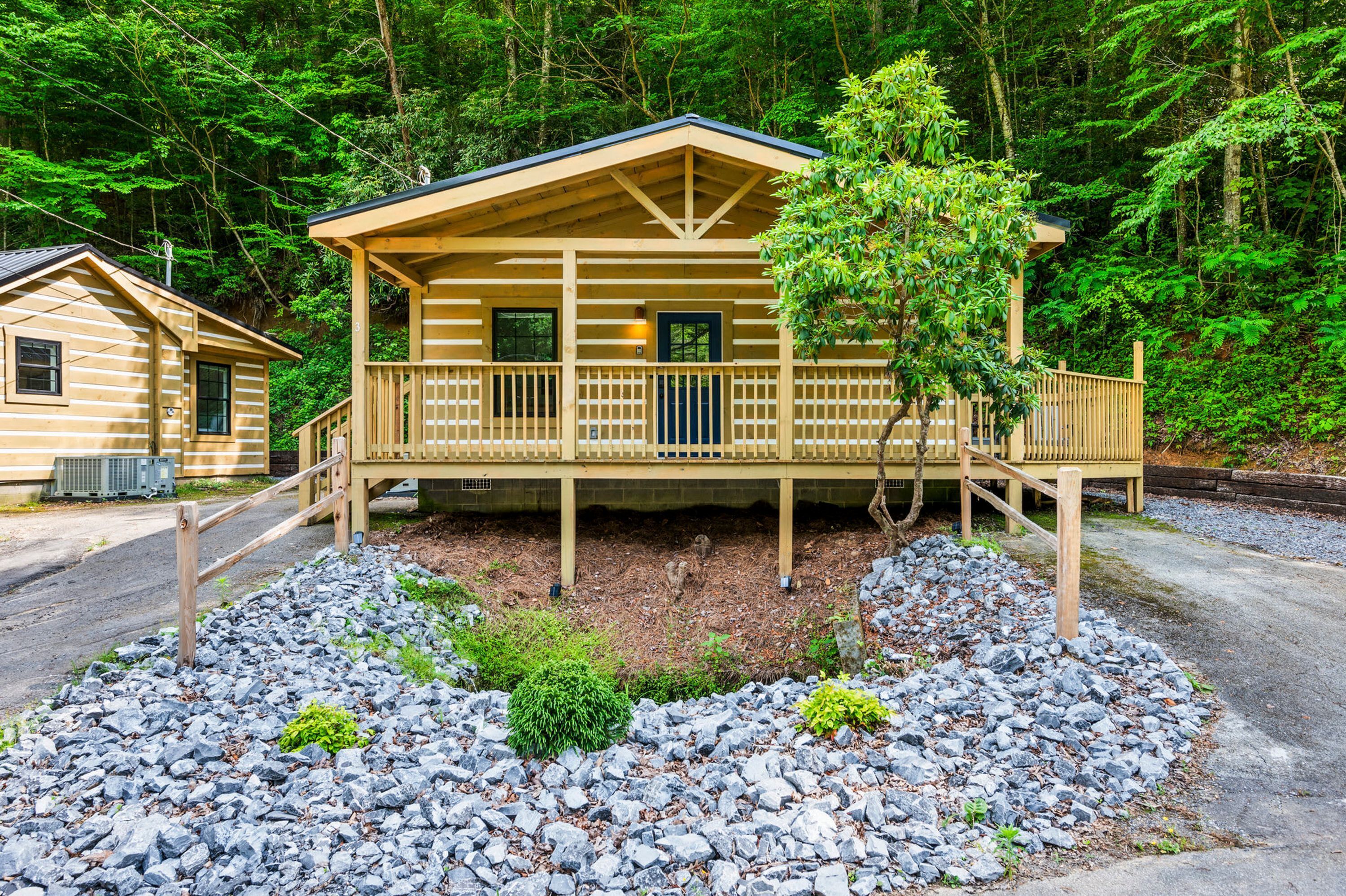 Eine Holzhütte mit Veranda, umgeben von einem felsigen Garten und dichtem Wald.