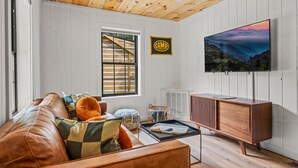 A cozy living room with a brown leather sofa, a wooden coffee table, and a mounted TV. - 2bdrm Cabin 3 Gburg Pet-friendly Firepit Games (Gatlinburg)