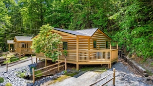 A cabin with a deck and a porch, surrounded by dense forest. - 2bdrm Cabin 3 Gburg Pet-friendly Firepit Games (Gatlinburg)
