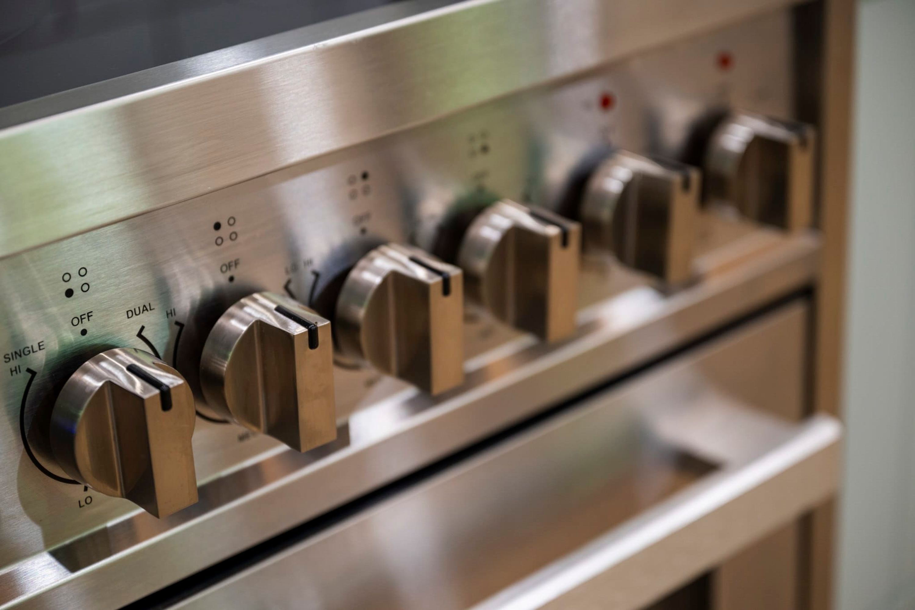 Gros plan d’un panneau de commande en acier inoxydable, doté de nombreux boutons et interrupteurs, probablement pour un appareil de cuisine.