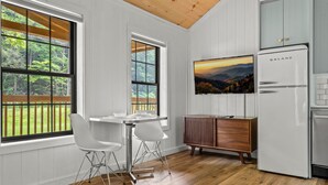 Eine moderne Küche mit weißen Schränken, einem Galanz-Kühlschrank, einem Holztisch mit weißen Stühlen und einem großen Fenster mit Blick auf Grünflächen.