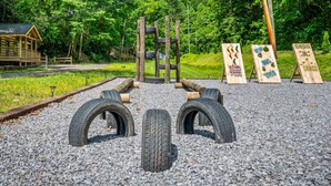 Ein Spielplatz mit Reifenhindernissen und Holzbrettern, beschriftet mit Aktivitäten wie 'BIG TOSS' und 'DUCK'.