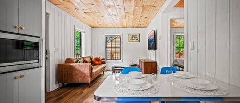 Una cocina moderna con armarios blancos, techo de madera y un comedor con una mesa blanca dispuesta para cuatro.