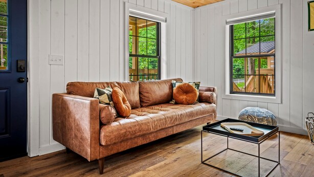 A room with a leather sofa, a coffee table, and two windows with views of greenery. - 2bdrm Cabin 2 Gburg Pet Friendly Fire Pit Game (Gatlinburg)