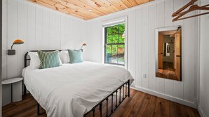 A bedroom with a wooden ceiling, white walls, a large bed, a window with a view of greenery, and a mirror on the wall. - 2bdrm Cabin 2 Gburg Pet Friendly Fire Pit Game (Gatlinburg)