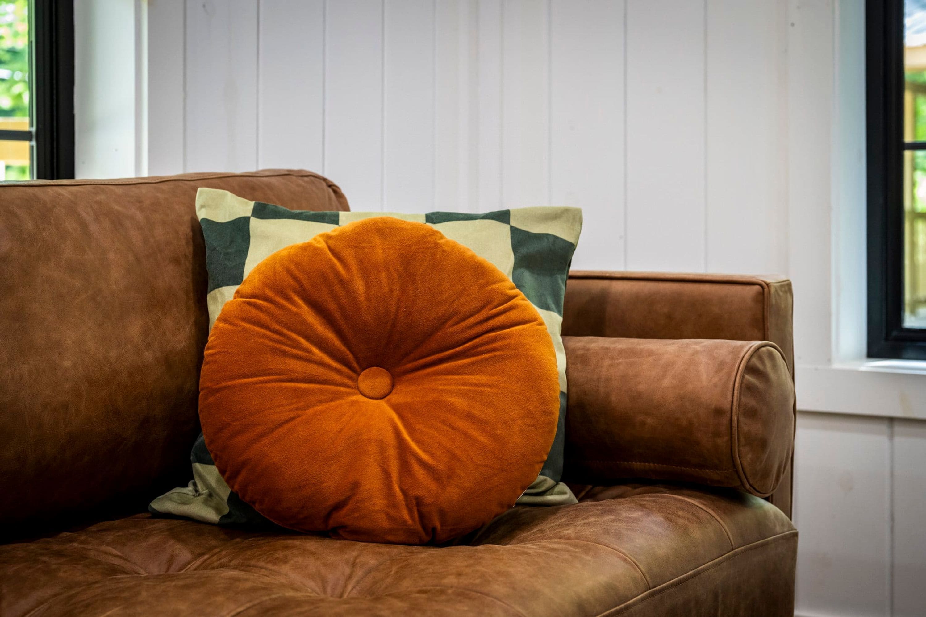 Un canapé en cuir marron avec un grand coussin orange et un oreiller à motifs.