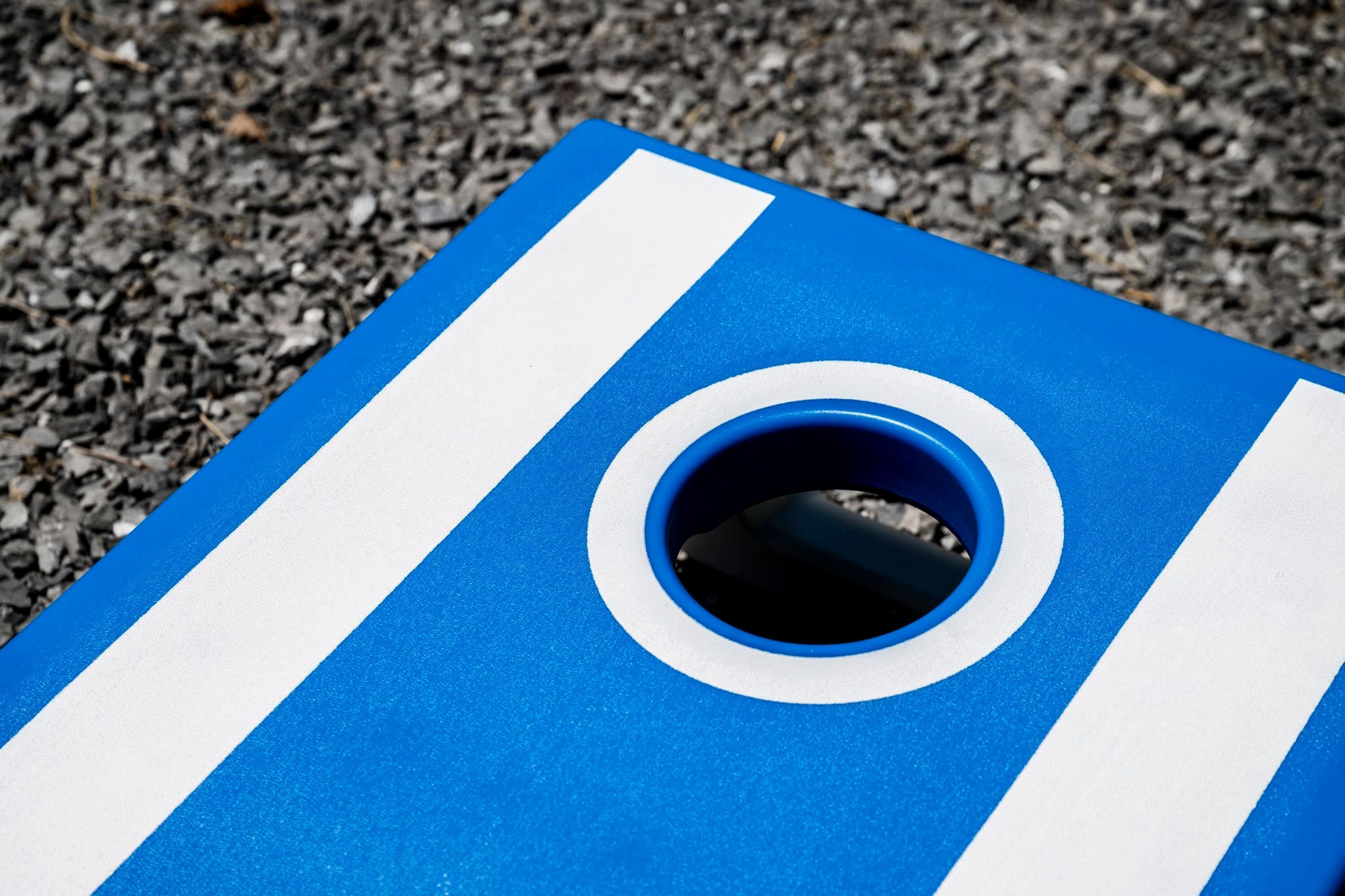A blue and white striped object with a circular hole on a gravel surface.