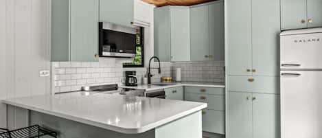 A modern kitchen with light green cabinets, a white island, and a Galanz refrigerator.