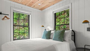 A bedroom with a large bed, two windows, and a small table.