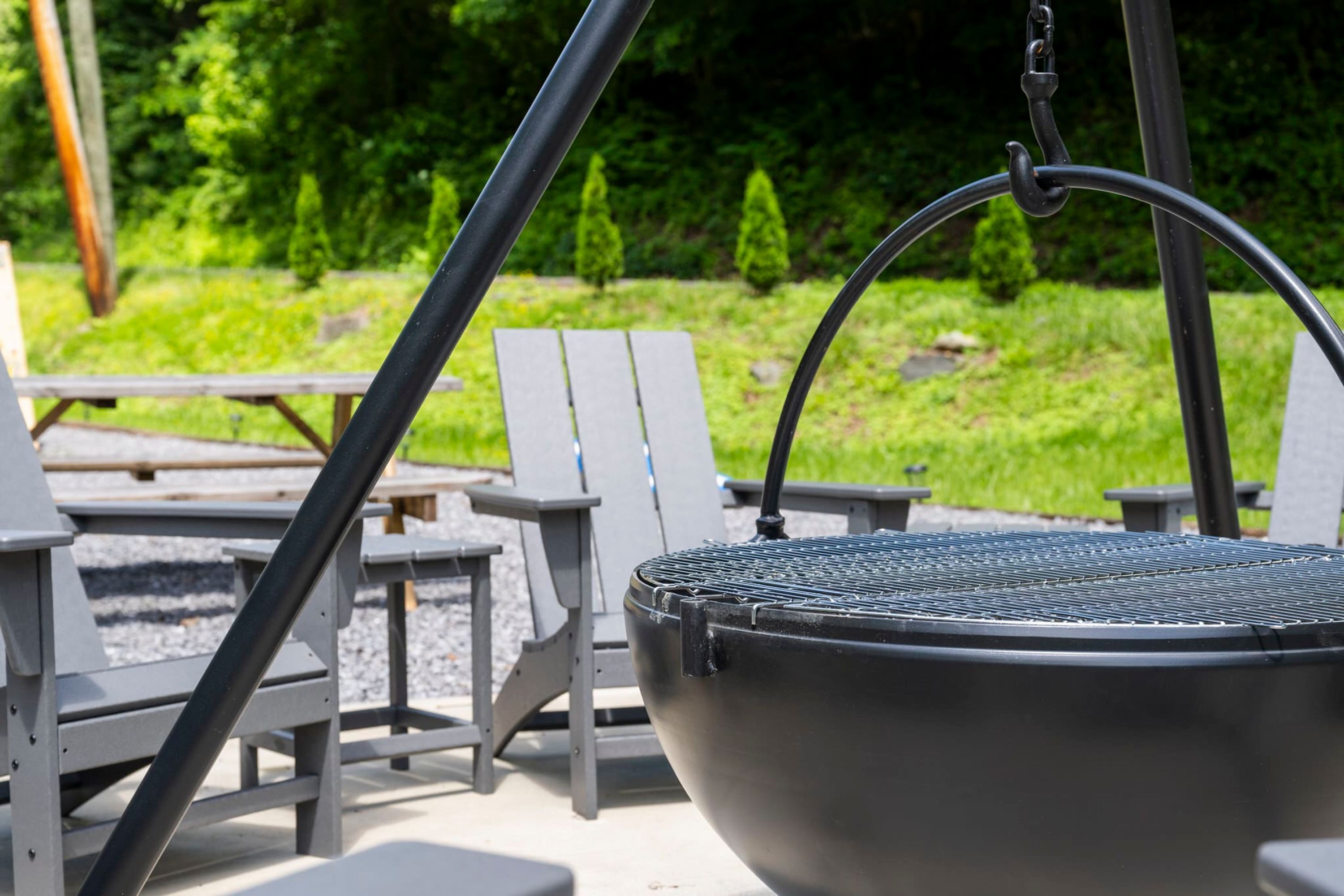 A barbecue grill with a metal grate, surrounded by outdoor seating including white chairs and tables.
