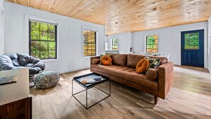 A spacious living room with a wooden ceiling, large windows, a brown leather sofa, and a coffee table.