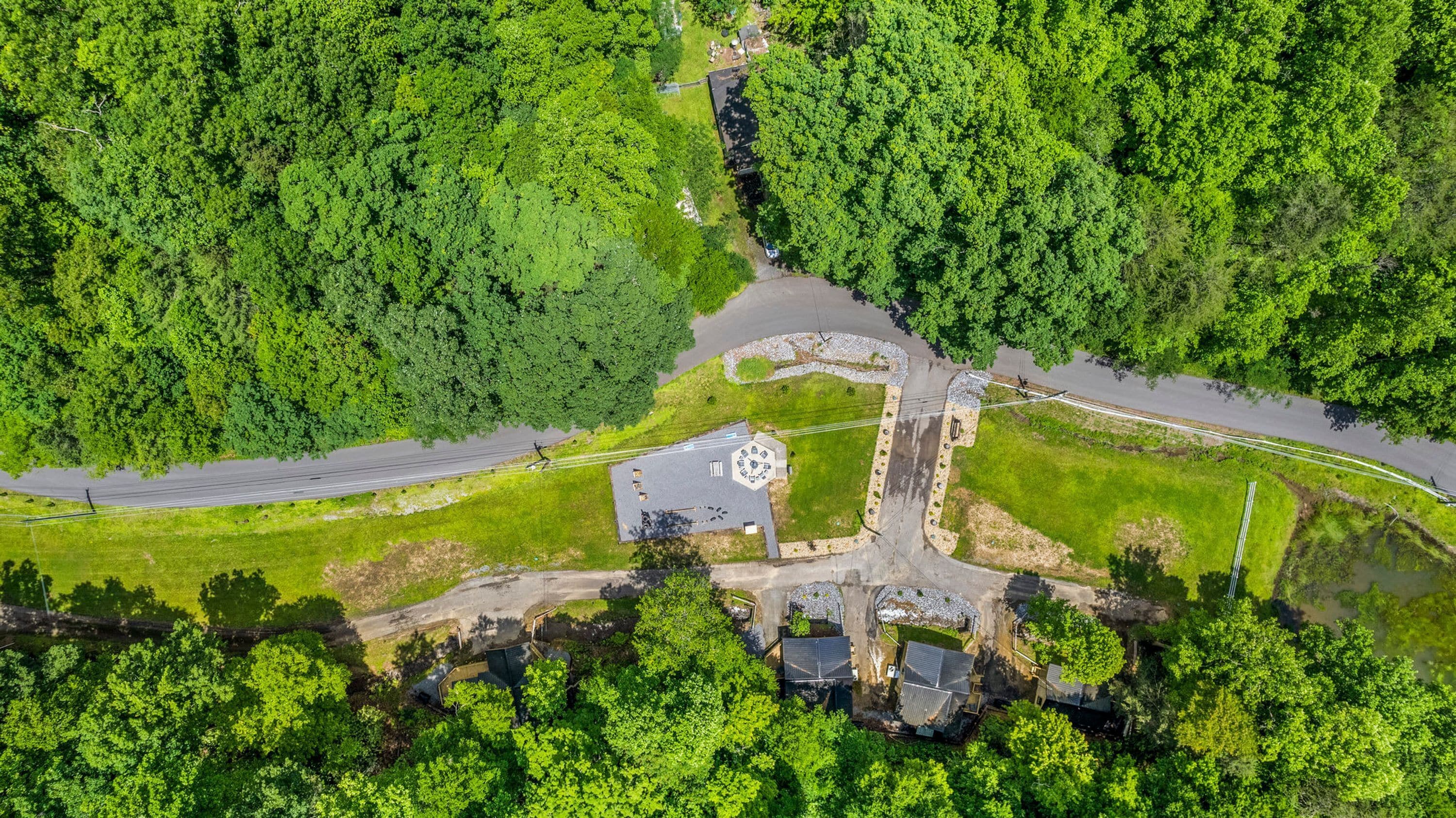 An aerial view of a park with a circular building, paved paths, and surrounding greenery.