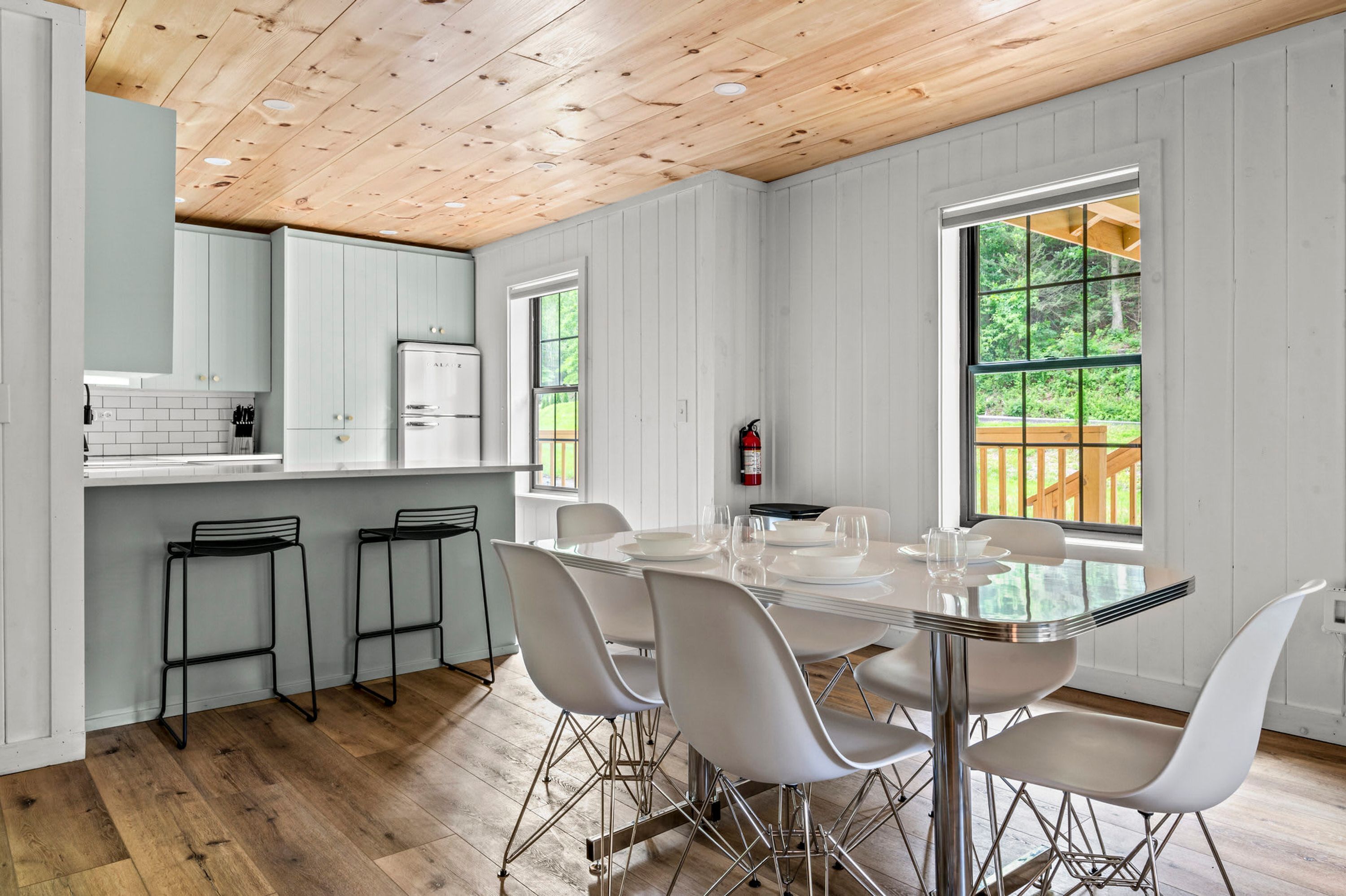A modern kitchen with white cabinets, a stainless steel refrigerator, and a dining area with a glass table and white chairs.