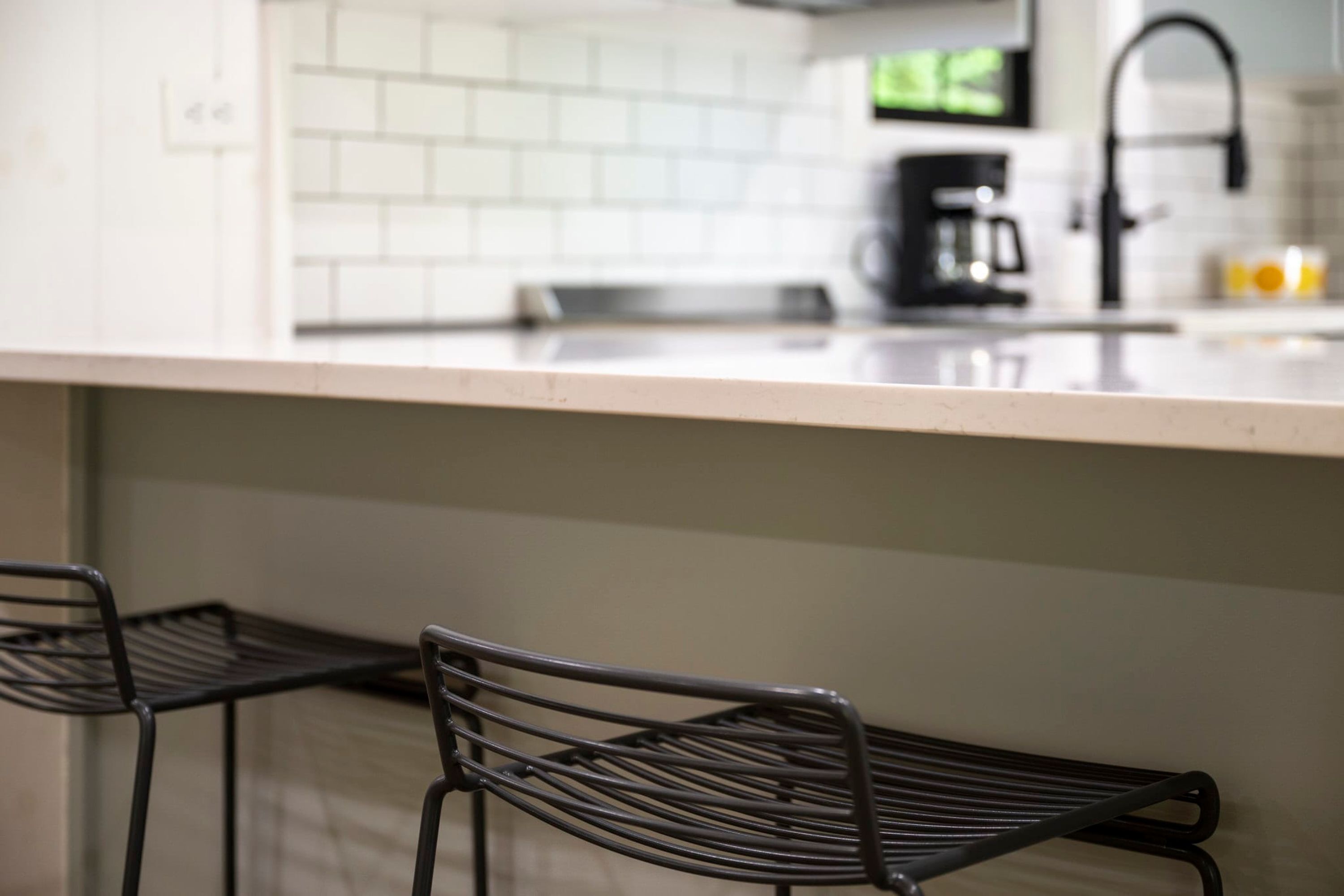 Una cocina moderna con azulejos blancos tipo metro, una campana extractora de acero inoxidable y una cafetera negra.